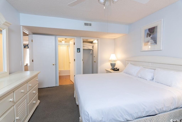 bedroom with a textured ceiling, dark carpet, a walk in closet, and ceiling fan