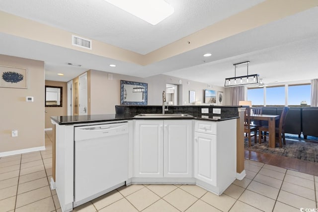 kitchen featuring dark countertops, visible vents, light tile patterned floors, white dishwasher, and a sink