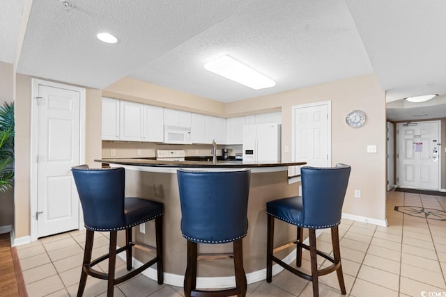 kitchen featuring white cabinetry, white appliances, a kitchen breakfast bar, and dark countertops