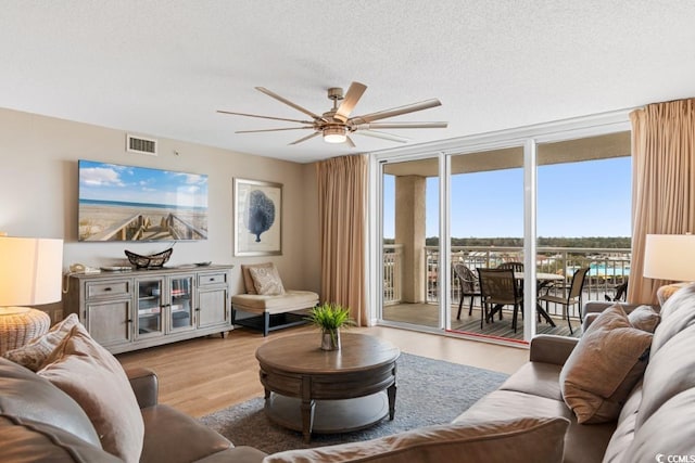 living room featuring visible vents, ceiling fan, expansive windows, wood finished floors, and a textured ceiling