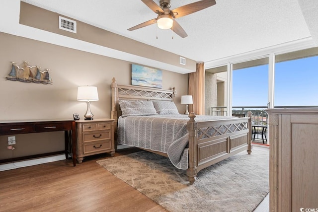 bedroom featuring floor to ceiling windows, wood finished floors, visible vents, and a textured ceiling