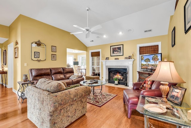 living room featuring a fireplace with flush hearth, a ceiling fan, visible vents, and light wood finished floors