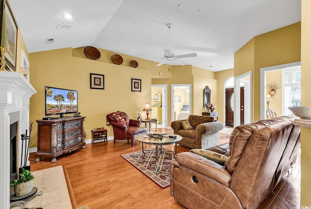 living room featuring light wood-type flooring, a fireplace with flush hearth, lofted ceiling, and visible vents