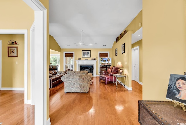 living room with light wood finished floors, a fireplace, ceiling fan, and vaulted ceiling