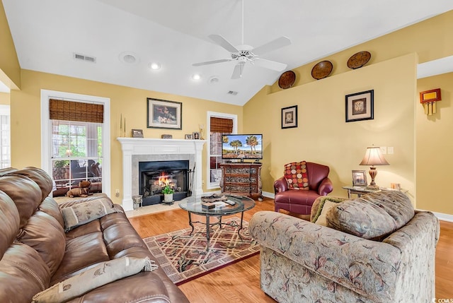 living area featuring light wood-type flooring, visible vents, a fireplace with flush hearth, baseboards, and vaulted ceiling