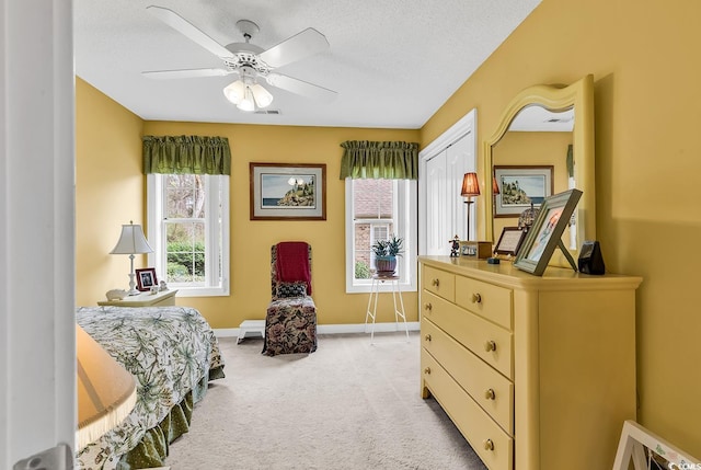 bedroom featuring visible vents, baseboards, ceiling fan, light colored carpet, and a textured ceiling