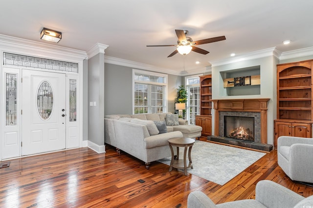living room featuring ceiling fan, ornamental molding, hardwood / wood-style flooring, a tile fireplace, and baseboards