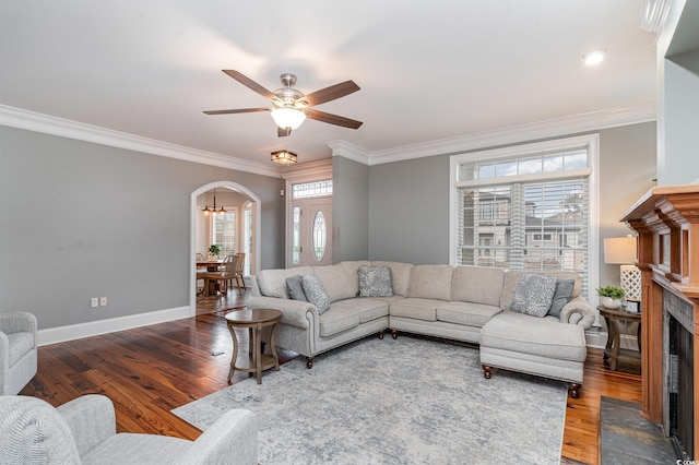 living area with a fireplace, wood finished floors, arched walkways, and ornamental molding