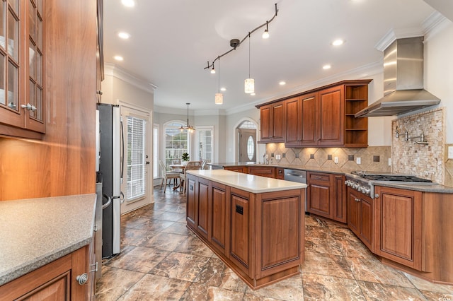 kitchen featuring ornamental molding, backsplash, appliances with stainless steel finishes, wall chimney exhaust hood, and brown cabinetry