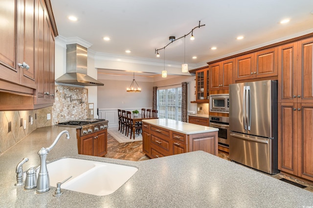 kitchen featuring brown cabinetry, a sink, appliances with stainless steel finishes, wainscoting, and wall chimney range hood