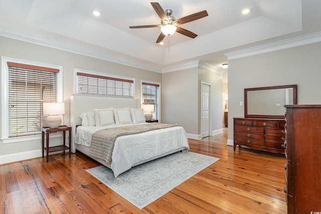 bedroom featuring multiple windows, light wood-type flooring, and a tray ceiling