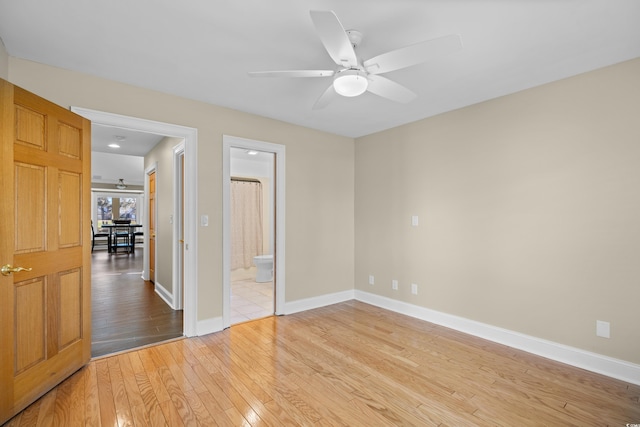 unfurnished bedroom featuring light wood-style flooring, baseboards, ensuite bath, and a ceiling fan