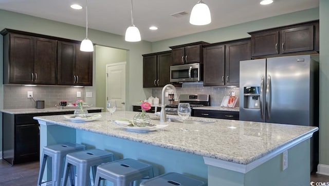 kitchen featuring appliances with stainless steel finishes, a sink, dark brown cabinets, an island with sink, and decorative backsplash
