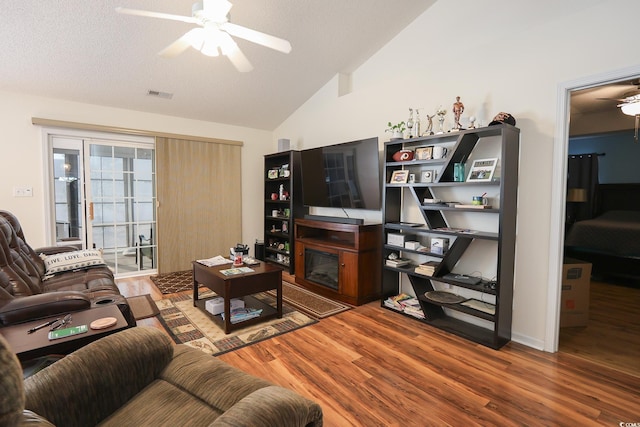 living area with visible vents, a ceiling fan, a glass covered fireplace, wood finished floors, and lofted ceiling