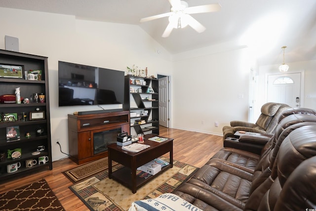 living area with wood finished floors, lofted ceiling, a glass covered fireplace, and a ceiling fan