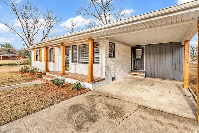 doorway to property featuring an attached carport, driveway, a porch, crawl space, and brick siding