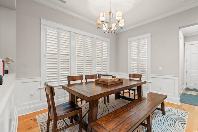 dining area with light wood finished floors, a notable chandelier, crown molding, and a wainscoted wall