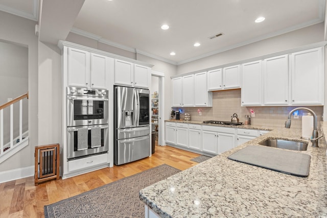 kitchen featuring light wood-type flooring, visible vents, ornamental molding, a sink, and appliances with stainless steel finishes