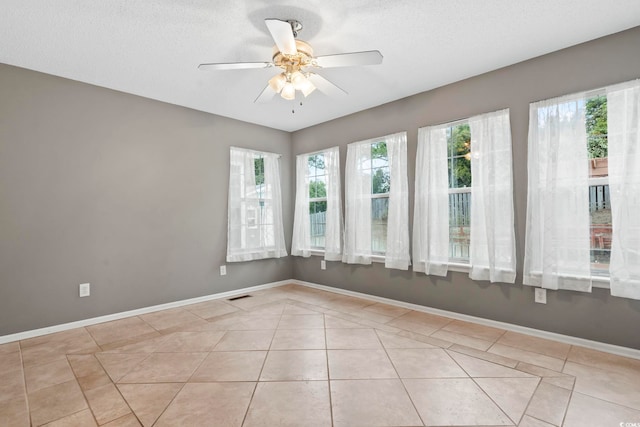 empty room with light tile patterned flooring, a healthy amount of sunlight, visible vents, and baseboards