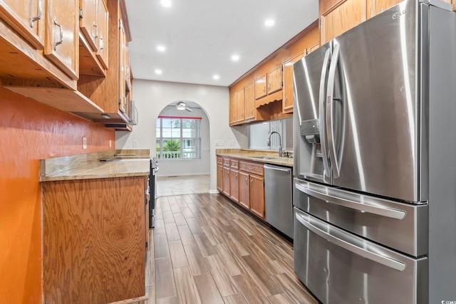 kitchen with wood finish floors, light countertops, arched walkways, stainless steel appliances, and a sink