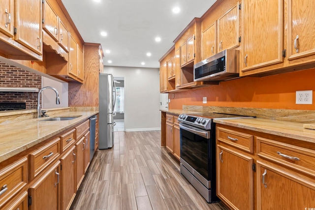 kitchen with brown cabinetry, appliances with stainless steel finishes, light wood-type flooring, and a sink