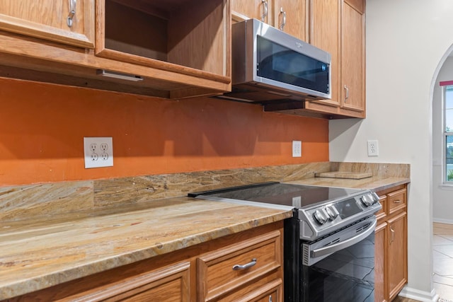 kitchen with tile patterned floors, brown cabinetry, arched walkways, and stainless steel appliances