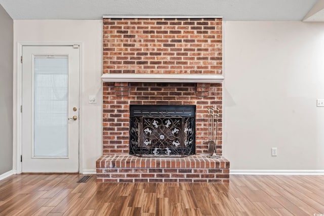 unfurnished living room with visible vents, a textured ceiling, wood finished floors, a fireplace, and baseboards