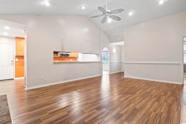 unfurnished living room with a ceiling fan, wood finished floors, arched walkways, baseboards, and vaulted ceiling