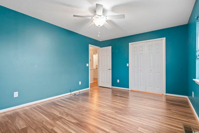 unfurnished bedroom featuring visible vents, baseboards, wood finished floors, a closet, and a textured ceiling