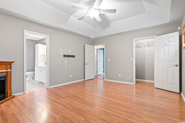 unfurnished bedroom featuring baseboards, a raised ceiling, light wood-style flooring, and a fireplace