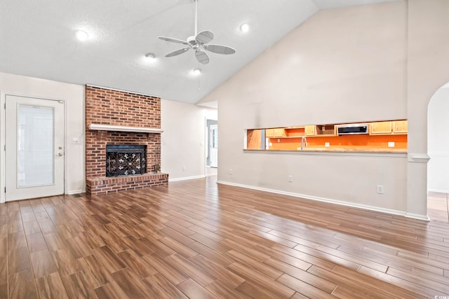 unfurnished living room with a brick fireplace, baseboards, ceiling fan, and wood finished floors