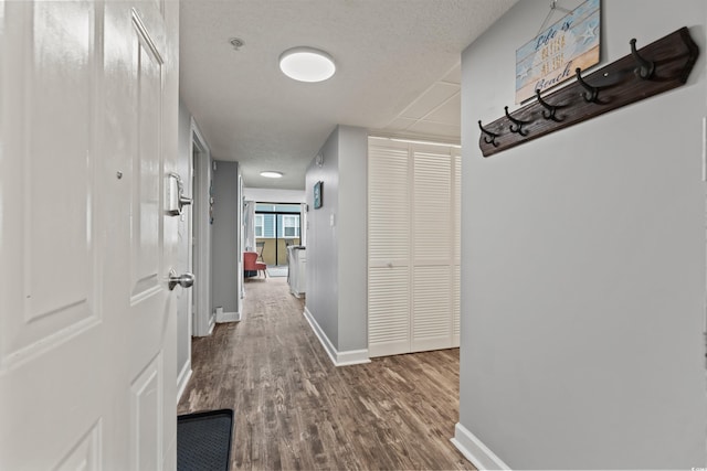 corridor with a textured ceiling, baseboards, and wood finished floors