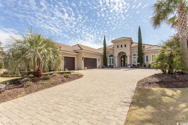 mediterranean / spanish-style home featuring stucco siding, a tiled roof, decorative driveway, and a garage