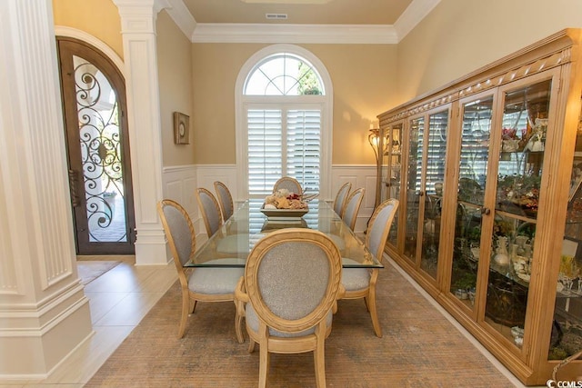 dining space featuring light tile patterned floors, wainscoting, ornate columns, and ornamental molding