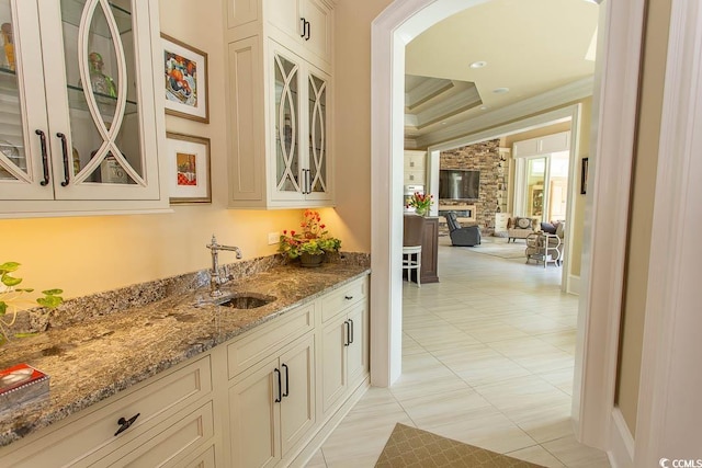 bar featuring ornamental molding, a sink, a tray ceiling, arched walkways, and a fireplace