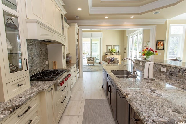 kitchen with ornamental molding, a sink, open floor plan, appliances with stainless steel finishes, and glass insert cabinets