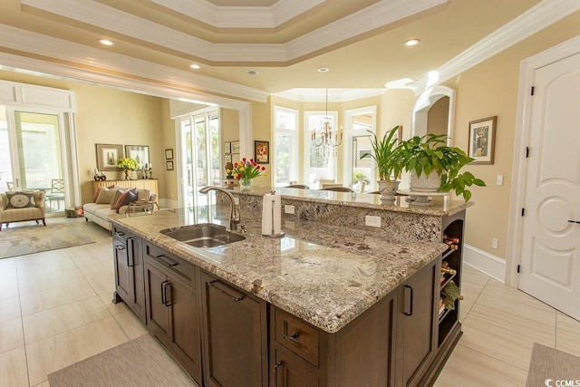 kitchen featuring light stone counters, a kitchen island with sink, ornamental molding, a sink, and open floor plan