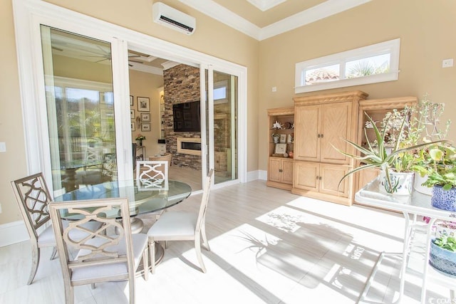 dining room with a wall unit AC, baseboards, ceiling fan, a stone fireplace, and crown molding