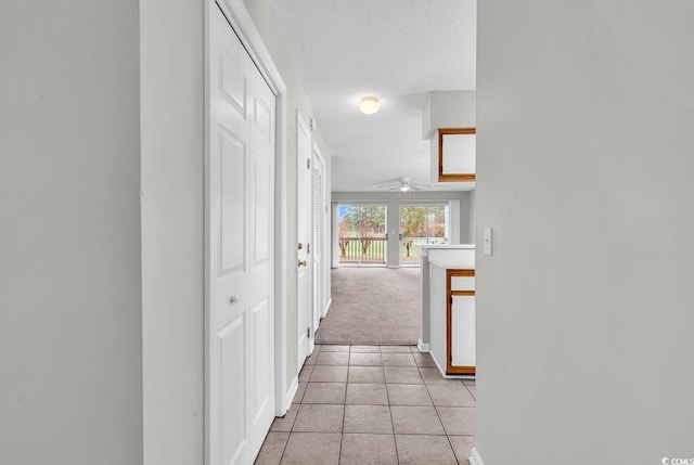 hall featuring light tile patterned floors, light colored carpet, baseboards, and a textured ceiling