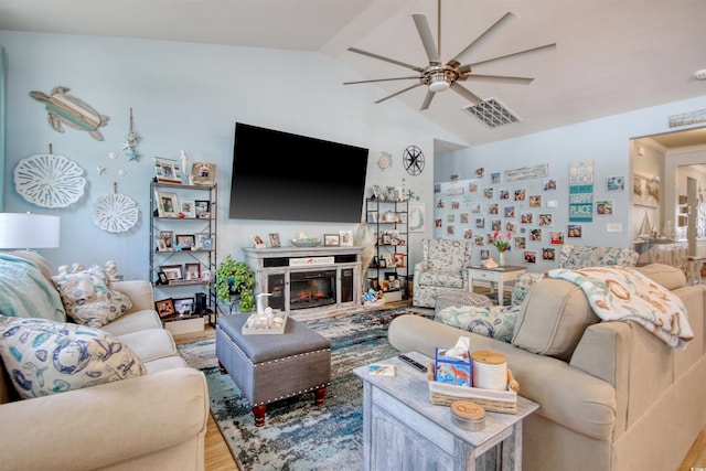 living area with wood finished floors, visible vents, ceiling fan, vaulted ceiling, and a glass covered fireplace