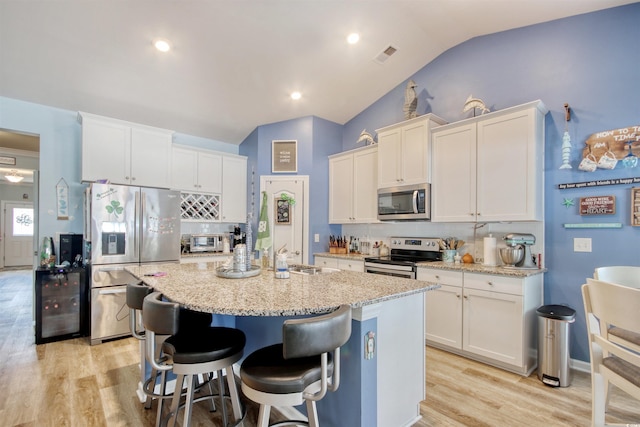 kitchen featuring visible vents, a kitchen island with sink, light wood-style flooring, stainless steel appliances, and lofted ceiling