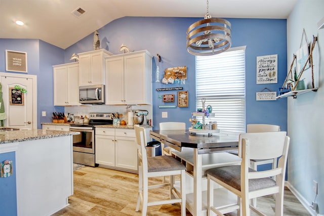 kitchen with visible vents, vaulted ceiling, white cabinets, light wood-style floors, and appliances with stainless steel finishes