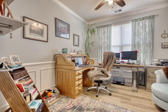 home office with light wood finished floors, visible vents, ceiling fan, ornamental molding, and wainscoting