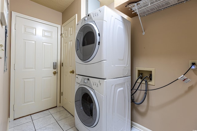 laundry room with a textured ceiling, stacked washer and clothes dryer, light tile patterned flooring, and laundry area