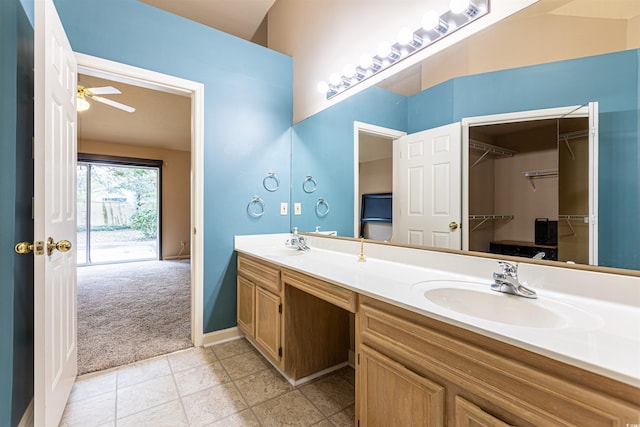 bathroom featuring a walk in closet, a sink, double vanity, baseboards, and ceiling fan