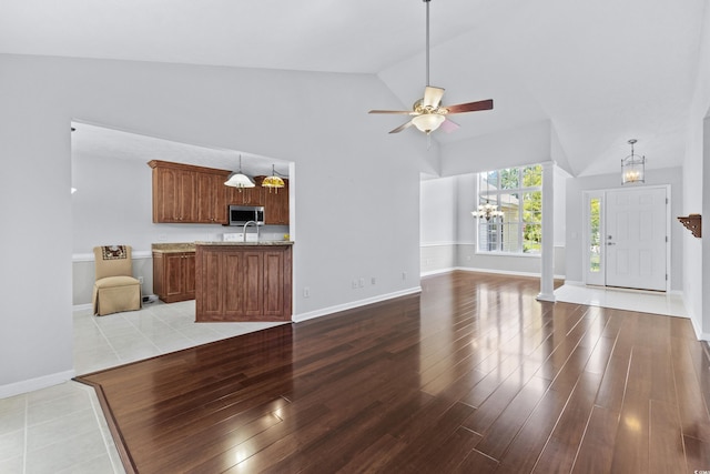 unfurnished living room featuring ceiling fan with notable chandelier, vaulted ceiling, wood finished floors, and baseboards