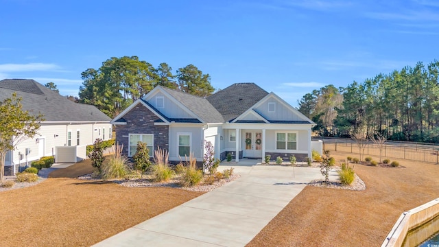 craftsman-style home with board and batten siding, fence, roof with shingles, french doors, and stone siding