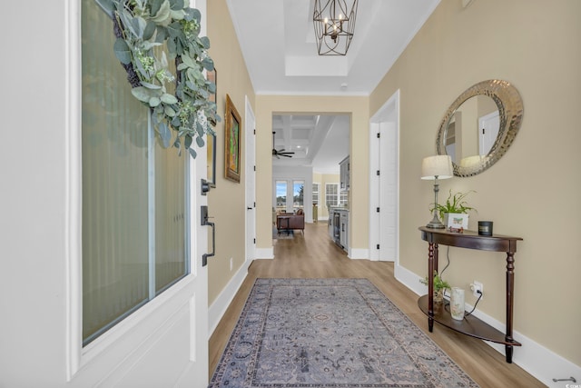 hallway featuring a notable chandelier, crown molding, baseboards, and wood finished floors