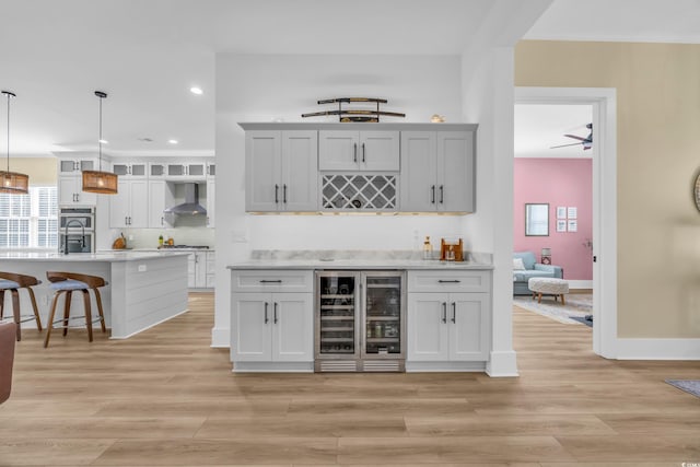 bar featuring light wood-style flooring, wine cooler, a bar, double oven, and wall chimney exhaust hood