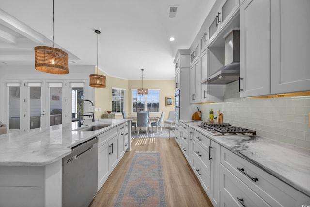 kitchen with a sink, tasteful backsplash, stainless steel appliances, light wood-style floors, and wall chimney range hood